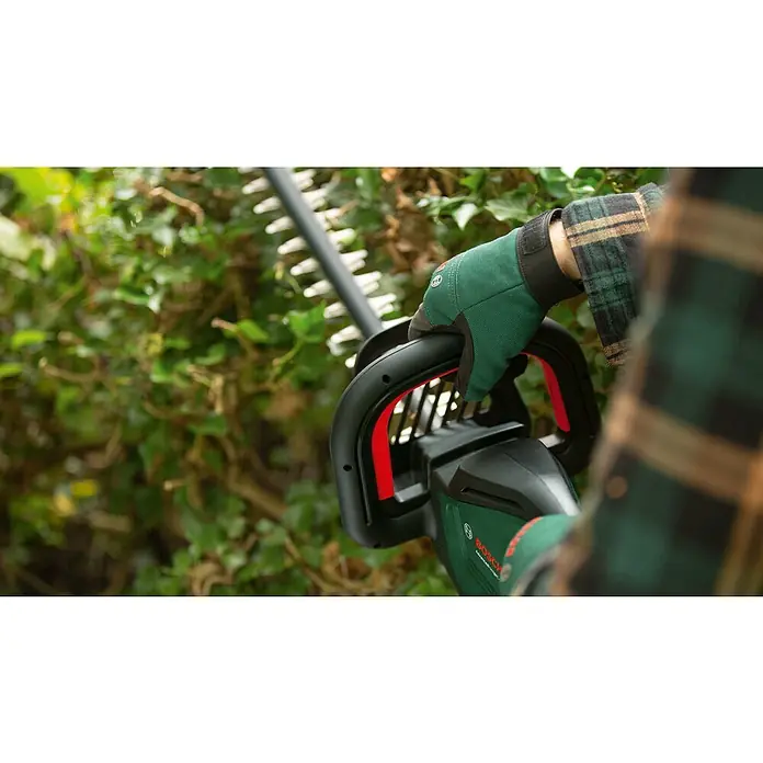 Bosch Power for All 36V Akku-Heckenschere AdvancedHedgeCut 36V-65-2836 V, Li-Ionen, Ohne Akku - Nahaufnahme einer Person, die mit einer Bosch Heckenschere eine Hecke schneidet, wobei der Fokus auf dem Werkzeug und dem grünen Handschuh liegt.