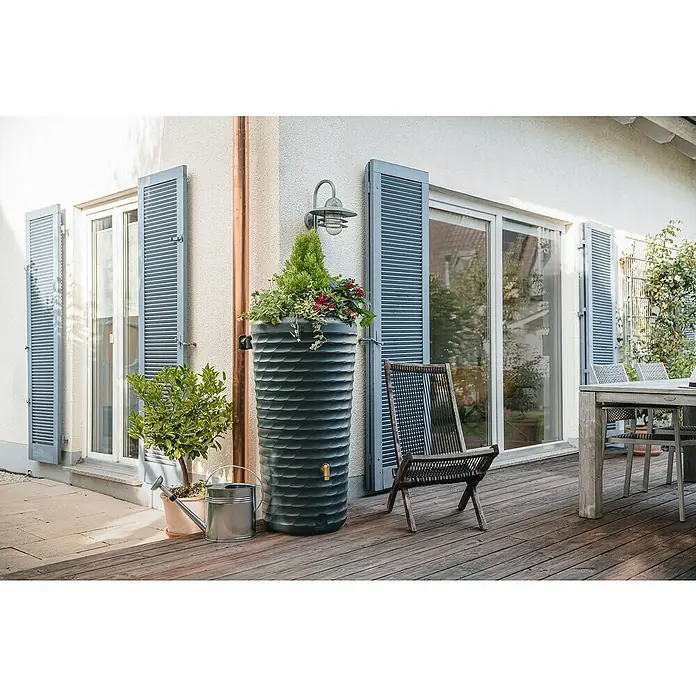 4rain Regenspeicher Jolie - 230 l, Graphitgrau, 1 Stk. - Ein grauer Regenspeicher steht auf einer Holzterrasse neben einem Stuhl. Der Regenspeicher ist mit Pflanzen bepflanzt und fängt Regenwasser auf.
