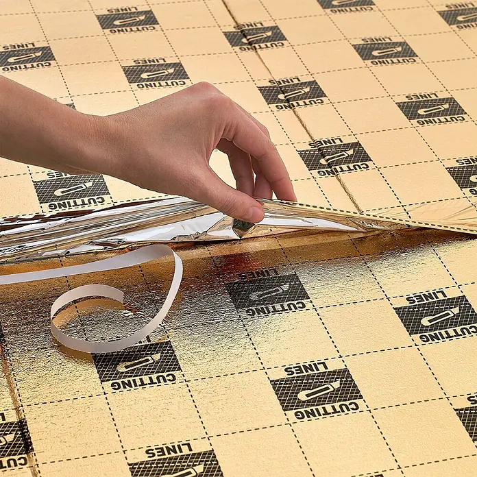 Dämmunterlage SPC & LVT - 10 m², Stärke: 1,5 mm - Nahaufnahme einer Hand, die eine goldene Dämmfolie mit aufgedruckten Schneidelinien abzieht.