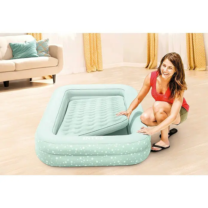 Intex Luftbett Reisebett für Kinder - L x B x H: 168 x 107 x 25 cm, Hellblau, Sicherheitsventil - Eine Frau kniet neben einer mintgrünen Intex-Luftmatratze mit Sternenmuster und separater Luftmatratze.