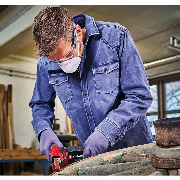 Einhell Expert Elektro-Bandschleifmaschine TC-BF 500 E - 500 W - Ein Mann arbeitet mit einer Einhell Bandschleifmaschine an einem Holzstück, geschützt durch Maske, Brille und Handschuhe.