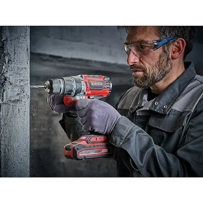 Einhell Power X-Change 18V Akku-Schlagbohrschrauber TP-CD 18/70 Li-i BL - Solo - 18 V, Ohne Akku, 70 Nm - Ein Mann bohrt mit einer Einhell Akku-Bohrmaschine Power X-Change in eine Betonwand. Schutzbrille und Handschuhe sind getragen.