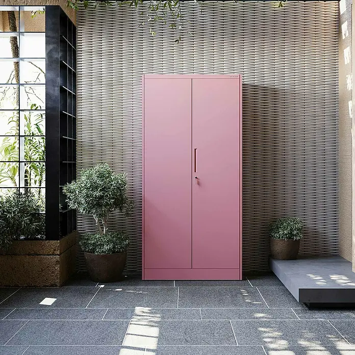 Jan Nowak Metall-Mehrzweckschrank Dawid - H x B x T: 185 x 90 x 45 cm, Rosa - Hoher rosa Metallschrank mit Doppeltüren, in einem Außenbereich mit Pflanzen und strukturierter Wand.