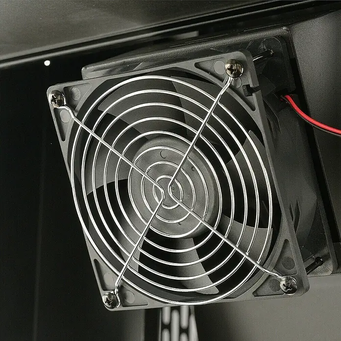 Masterbuilt Holzkohlegrill Gravity 600 - Grillfläche (B x T): 56 x 44 cm, Schwarz - Schwarzer Lüfter mit silbernem Metallschutzgitter und vier Schrauben, installiert in einem dunklen Gehäuse mit roten und schwarzen Kabeln.