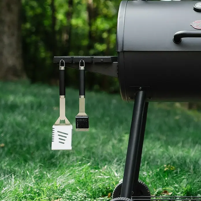 Char-Griller Holzkohlegrill inkl. Offset-Smoker - Grillfläche (B x T): 79 x 44 cm, Schwarz - Ein schwarzer Außengrill mit einem silbernen Spatel und einem Pinsel, die an seiner Seite hängen.
