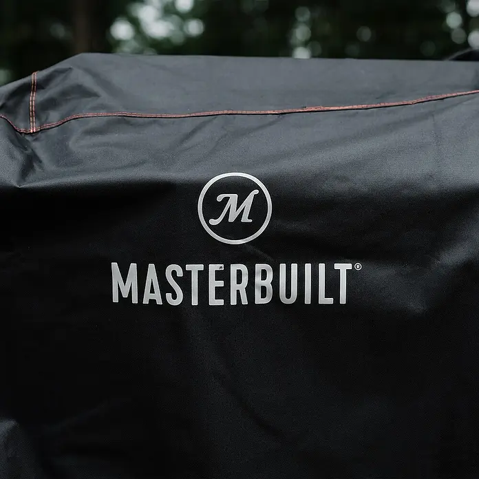 Char-Griller Grill-Schutzhülle - Passend für: Gravity Series 1050, 1150 und XT Digital Charcoal Grill + Smokern - Schwarze Masterbuilt Grillabdeckung aus strapazierfähigem Stoff mit weißem Logo und orangefarbenen Nähten, draußen gezeigt.