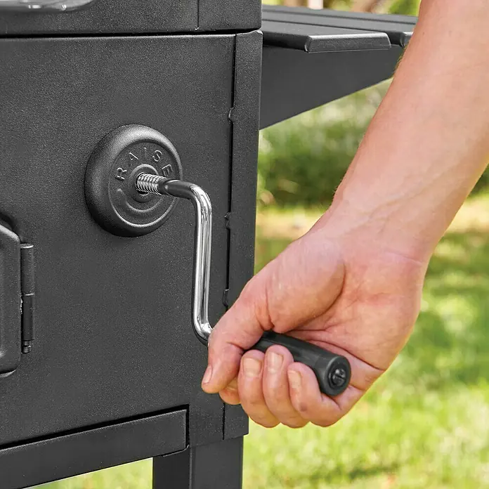 Char-Griller Holzkohlegrill Traditional - Grillfläche (B x T): 76 x 44 cm, Schwarz - Eine Hand dreht die Kurbel eines schwarzen Metallgrills mit „RAISE“-Prägung, um den internen Mechanismus zu verstellen.