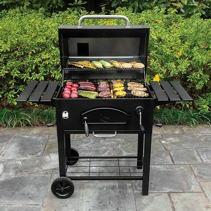 Char-Griller Holzkohlegrill Traditional - Grillfläche (B x T): 76 x 44 cm, Schwarz - Schwarzer Holzkohlegrill mit kochendem Essen auf den Rosten, darunter Burger, Würstchen, Gemüse und Brötchen. Er hat Seitenablagen und Räder.