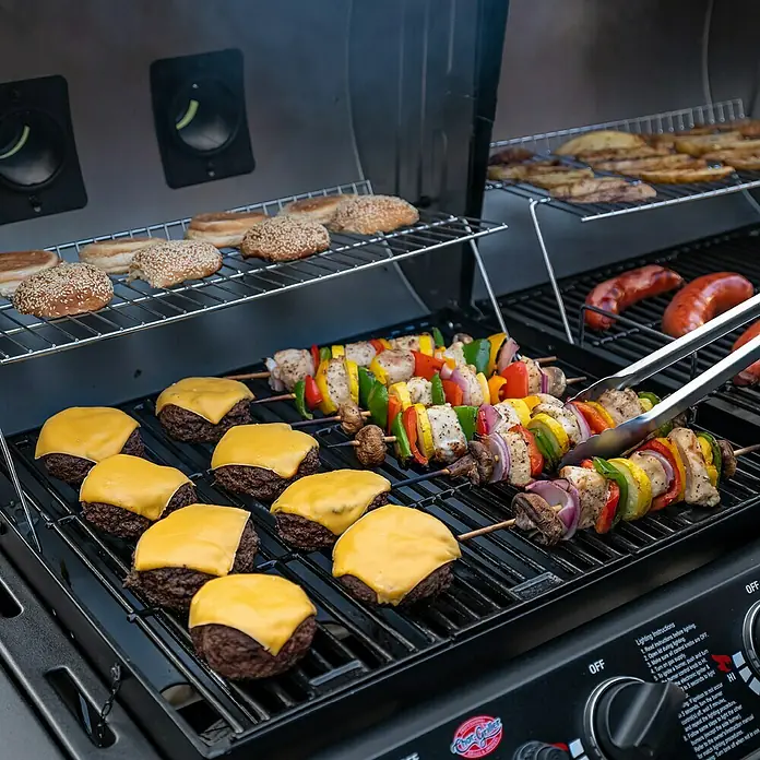 Char-Griller Hybrid-Grill Double Play Gas & Holzkohle - Grillfläche (B x T): 101 x 50 cm, 15,48 kW - Schwarzer Char-Griller Gasgrill mit brutzelnden Cheeseburgern, Hähnchenspießen, Würstchen und Brötchen, bereit zum Essen.