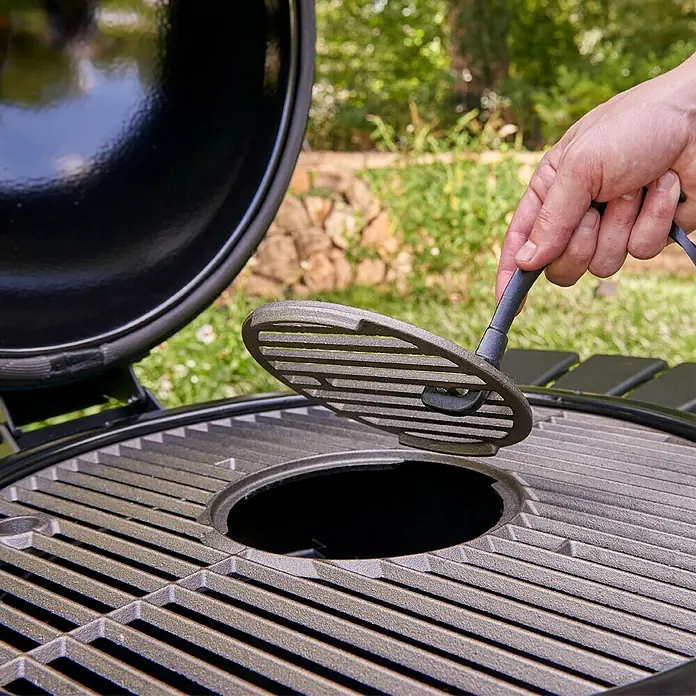 Char-Griller Holzkohlegrill Akorn Kamado - Durchmesser Grillfläche: 50 cm, Schwarz - Eine Hand entnimmt mit einem Werkzeug einen dunkelgrauen gusseisernen Grillrost-Einsatz aus einem großen Grill.
