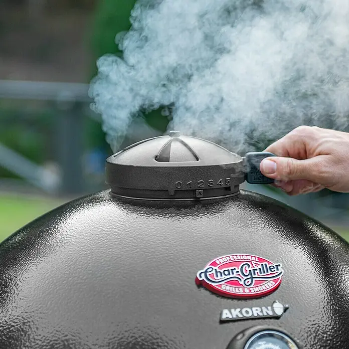 Char-Griller Holzkohlegrill Akorn Kamado - Durchmesser Grillfläche: 50 cm, Schwarz - Dunkelgrauer Char-Griller Akorn Grill mit Rauch aus der oberen Lüftung, während eine Hand die Klappe einstellt.