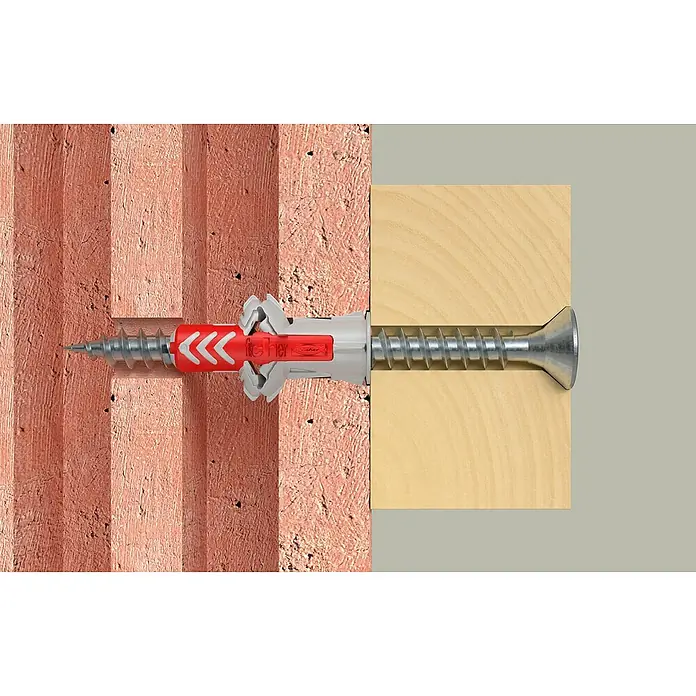 Fischer Schrauben- & Dübel-Set DuoPower 6,8,10 S - Geeignet für: Voll- und Lochbaustoffe, Nylon, Stahl, 18 Stk. - Ein Dübel mit Schraube befestigt ein Holzbrett an einer roten Ziegelwand und bietet sicheren Halt.