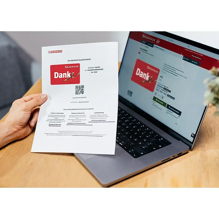 Gutscheinkarte - Zum Selbstausdruck, 10 Euro, Danke - Ein Foto zeigt eine Person, die einen Bauhaus-Gutschein vor einen Laptop hält, auf dem die Bauhaus-Website mit dem gleichen Gutschein angezeigt wird.