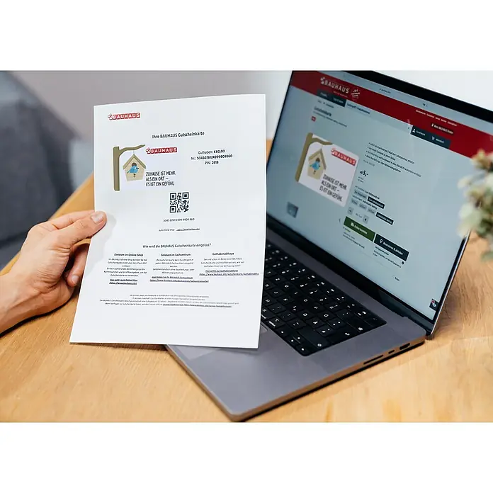 Gutscheinkarte - Zum Selbstausdruck, Individueller Betrag, Zuhause ist mehr - Ein Gutschein von Bauhaus wird neben einem Laptop präsentiert, der die Bauhaus-Webseite anzeigt.