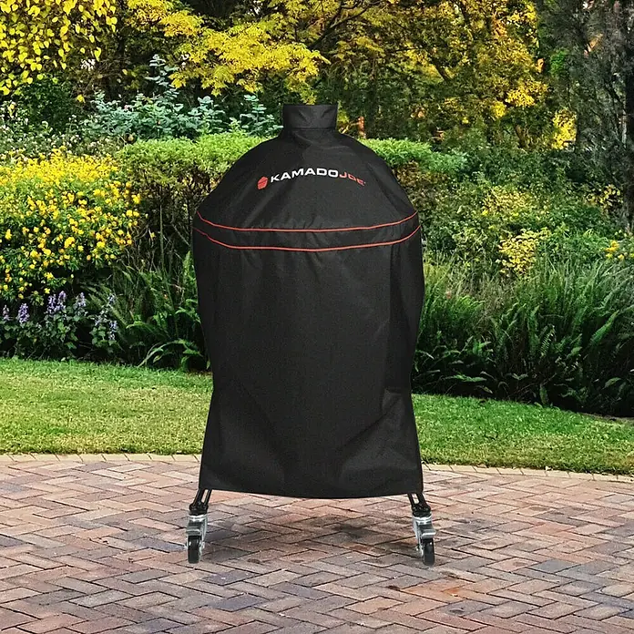 Kamado Joe Funda protectora para barbacoa - Específico para: Barbacoa de carbón Kamado Joe Classic - Funda negra Kamado Joe para barbacoa con borde rojo, protegiendo una barbacoa con ruedas en un patio exterior.
