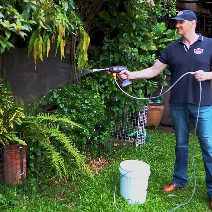 Hidrolimpiadora de alta presión de batería Hydroblast - 9,5 bar, 21 V, Capacidad de bombeo: 210 l/h - Hombre opera una máquina de limpieza portátil conectada a un cubo al aire libre, ideal para jardinería y mantenimiento exterior.