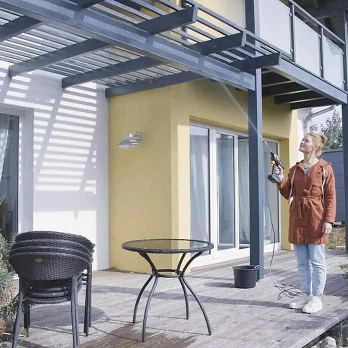 Hidrolimpiadora de alta presión de batería Hydroblast - 9,5 bar, 21 V, Capacidad de bombeo: 210 l/h - Una mujer usa una hidrolimpiadora portátil para limpiar el patio de una casa.
