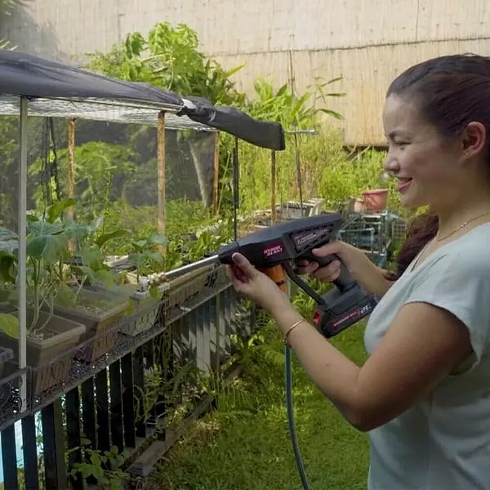 Hidrolimpiadora de alta presión de batería Hydroblast - 9,5 bar, 21 V, Capacidad de bombeo: 210 l/h - Mujer utiliza una hidrolavadora HYPER TOUGH para regar su jardín.