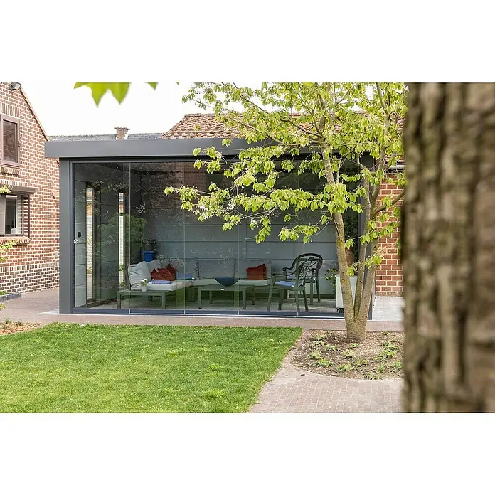 Telluria Pérgola estándar Singolo 4836 con ventanas - Medidas ext. (An x Pr): 508 x 388 cm, Acero, Antracita, Sin set - Una moderna sala de terraza con paredes de vidrio y elegantes muebles de jardín, rodeada de vegetación y árboles.