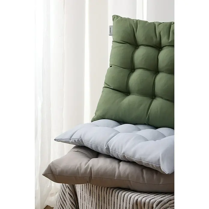 Cojín para silla water resist - 45 x 45 x 5 cm, Verde - Una pila de cojines de asiento acolchados de colores, con el verde actuando como respaldo, están en un taburete con una cubierta a rayas, frente a una cortina.