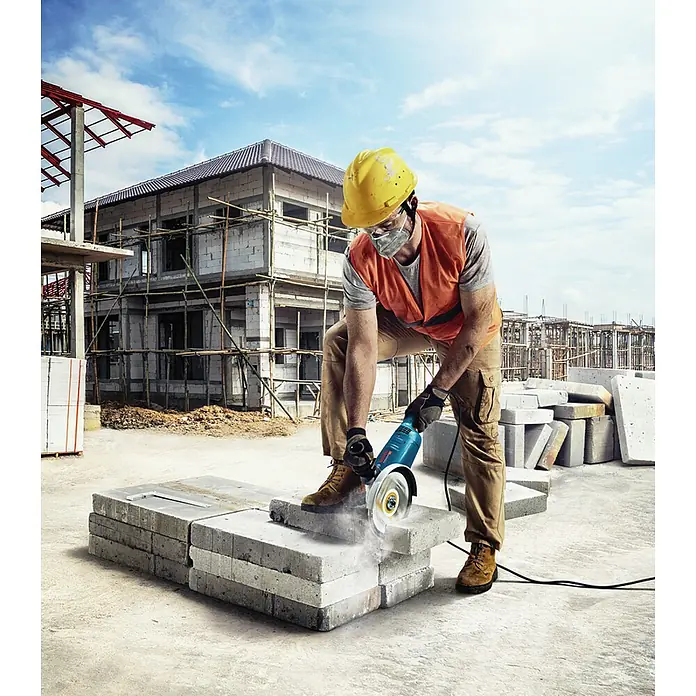 Bosch Professional Elektro-Winkelschleifer GWS 22-230 J - 2.200 W, Durchmesser Scheibe: 230 mm, Leerlaufdrehzahl: 6.500 U/min - Ein Bauarbeiter schneidet mit einer Bosch-Flex Steine auf einer Baustelle, um sie für den Bau zuzuschneiden.