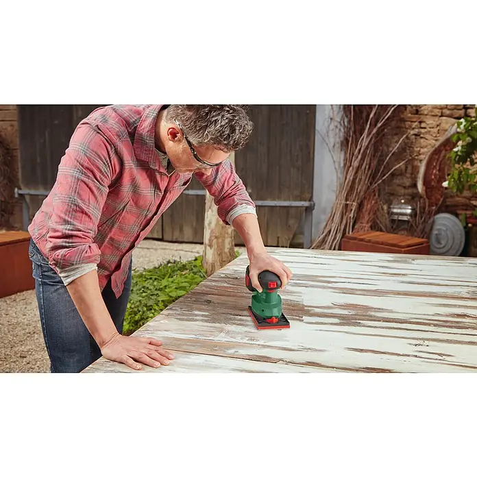 Bosch Power for All 18V Akku-Deltaschleifer Universal Sander 18V-10 - 18 V, Ohne Akku, Leerlaufschwingzahl: 12.000 U/min - 22.000 U/min - Ein Mann schleift eine Tischplatte mit einem Bosch-Multischleifer. Der Schleifer ist grün mit einem schwarzen Griff und einer roten Schleifplatte.