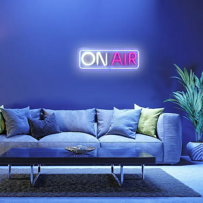 Just Light LED-Dekoleuchte Neon On Air - Neon On Air, L x B x H: 8,5 x 29,5 x 24 cm, Batteriebetrieben - Ein neonleuchtendes "ON AIR"-Schild hängt über einem Sofa in einem stilvollen Wohnzimmer, das eine moderne und einladende Atmosphäre schafft.