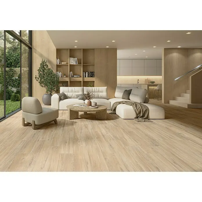 Pavimento porcelánico Elemental - 23 x 120 cm, Natur, Mate - Luminoso salón con suelos de madera, un sofá blanco y sillones, complementado con una elegante mesa de centro. La iluminación crea un ambiente cálido.