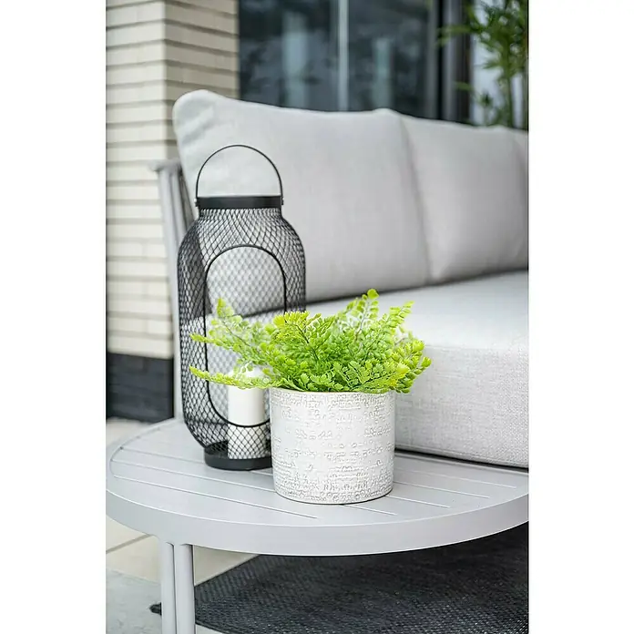Garden Impressions Loungemöbel-Set Frigole - 5 -tlg., Aluminium, Taupe/Sand - Runder grauer Outdoor-Couchtisch auf einer Terrasse, dekoriert mit einer schwarzen Laterne und einer grünen Topfpflanze.