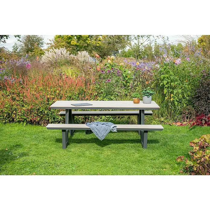 Garden Impressions Picknicktisch Bell - L x B x H: 200 x 178 x 75 cm, Aluminium, Vironwood, Schwarz/Hellbraun - Gartentisch-Bank-Kombination aus hellem Holz mit grauem Gestell in einer üppigen Gartenumgebung. Laptop und Pflanzen auf dem Tisch, blaue Jacke auf der Bank.