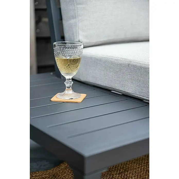Garden Impressions Loungemöbel-Set Prinos - 4 -tlg., Aluminium, Grau/Schwarz - Grauer Outdoor-Tisch mit Rillen, auf dem ein Glas vor einem hellgrauen Polster steht.