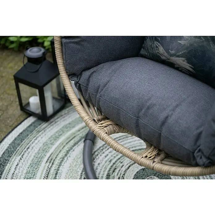 Garden Impressions Hängesessel Panama - L x B x H: 100 x 100 x 200 cm, Kunststoff, Schwarz/Beige - Nahaufnahme eines beigen Outdoor-Korbsessels mit dunkelgrauen Stoffkissen auf gestreiftem Outdoor-Teppich neben einer schwarzen Laterne.
