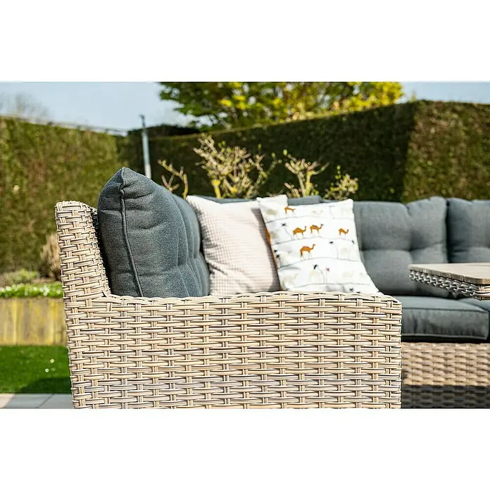 Garden Impressions Loungemöbel-Set Seagull - Linksausrichtung - Nahaufnahme eines beigefarbenen Rattan-Outdoor-Sessels mit dunkelgrauen Kissen und Zierkissen in einem sonnigen Außenbereich.