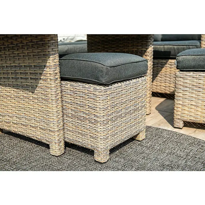 Garden Impressions Loungemöbel-Set Seagull - Rechtsausrichtung - Outdoor-Hocker aus hellbraunem und grauem Polyrattan mit dunkelgrauem Kissen, auf einem strukturierten Teppich.
