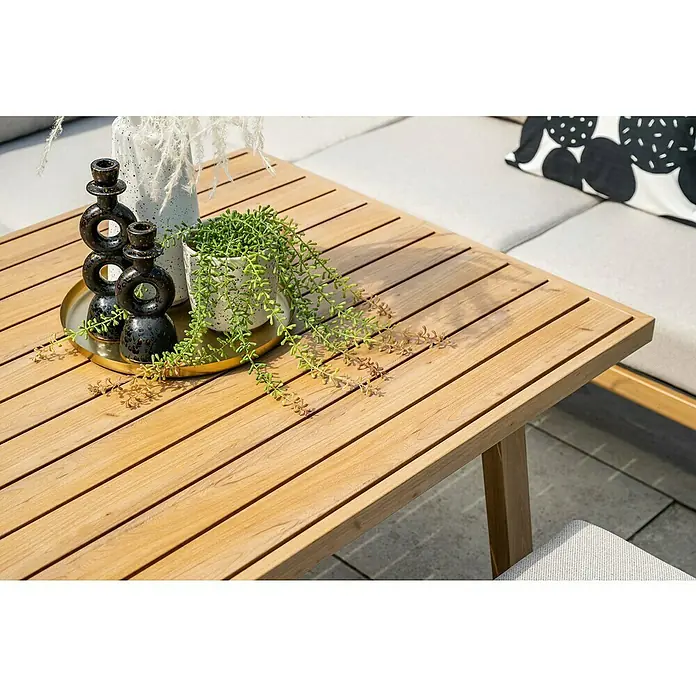 Garden Impressions Loungemöbel-Set Decala -  - Ein heller Holztisch mit Latten für den Außenbereich, dekoriert mit einer Pflanze und Kerzenständern, steht auf einer Terrasse neben einem Sofa.