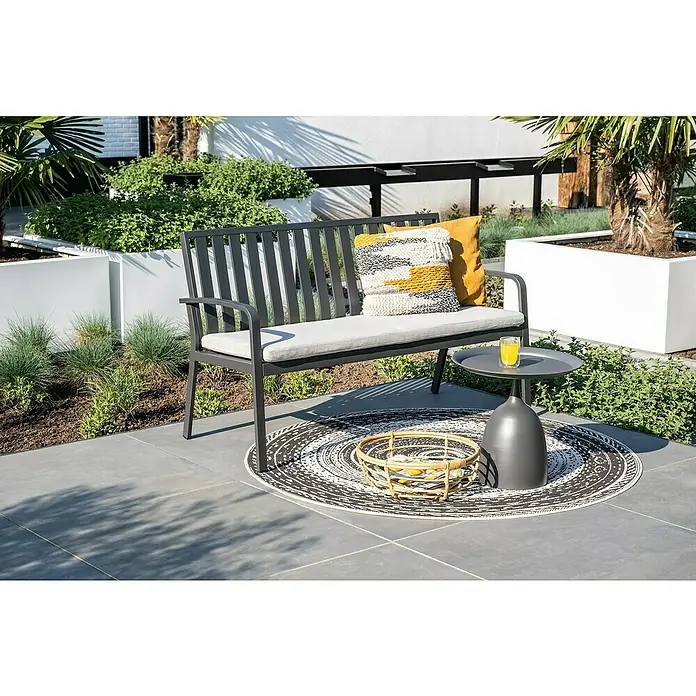 Garden Impressions Gartenbank Pisa - B x T x H: 150 x 52,5 x 89,5 cm, Aluminium, Polyester, Schwarz - Dunkelgraue Gartenbank aus Metall mit hellgrauen Polstern und Zierkissen, auf einer Terrasse mit Teppich und Beistelltisch.