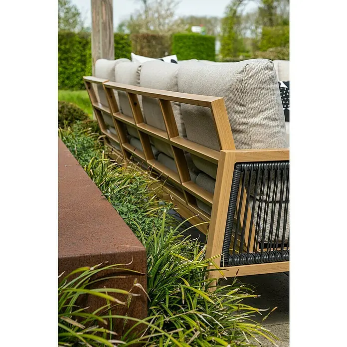 Garden Impressions Loungemöbel-Set Decala -  - Modernes Outdoor-Sofa mit hellem Holzrahmen, grauen Polstern und schwarzen Webakzenten, in einem Garten platziert.