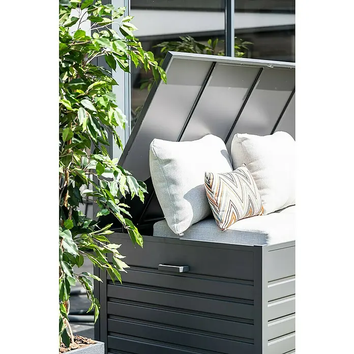 Garden Impressions Auflagenbox Primo - 155 x 97 x 825 cm, Metall, Dunkelgrau - Dunkelgraue Latten-Gartenbank mit offenem Deckel, hellen Kissen und gemustertem Kissen, auf einer Terrasse.