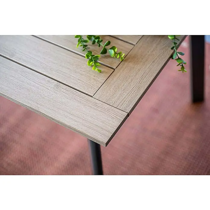 Garden Impressions Gartentisch Vigo - L x B x H: 160 x 90 x 73 cm, Aluminium, Vironwood, Rechteckig, Schwarz/Weiß - Helle Tischplatte in Holzoptik mit Lamellen und einer grünen Pflanze. Dunkles Tischbein auf gemustertem Boden sichtbar.
