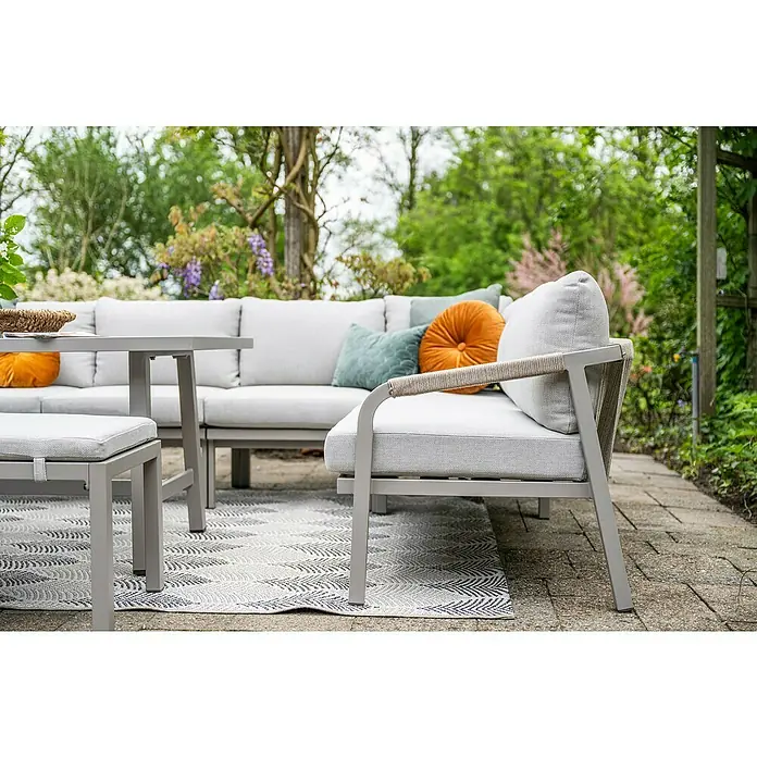 Garden Impressions Loungemöbel-Set Monti - 5 -tlg., Aluminium, Polyester, Grau - Eine hellgraue Outdoor-Lounge-Gruppe mit Sofa, Sessel, Tisch und Hocker, mit bunten Kissen, auf einem gemusterten Teppich auf einer Terrasse.