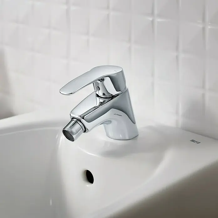 Roca Eos-N Grifo monomando de bidé - Cromo, Brillante - Primer plano de un brillante grifo de bidé Roca cromado montado sobre un lavabo de cerámica blanca, mostrando su diseño elegante y moderno.