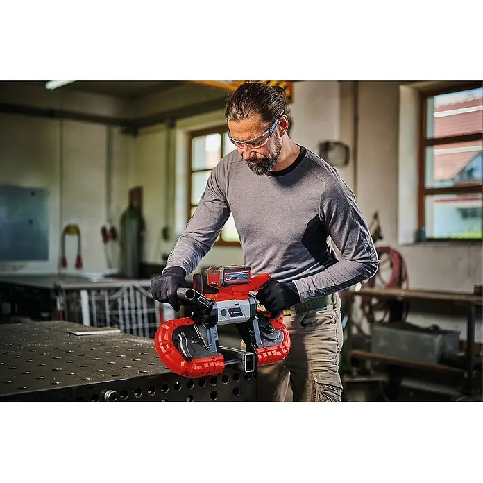 Einhell Power X-Change 18V Akku-Bandsäge TE-MB 18/127 Li-Solo - 18 V, Ohne Akku, Leerlaufdrehzahl: 240 U/min - Mann in Werkstatt benutzt Einhell Akku-Bandsäge zum Schneiden von Metall, trägt Schutzbrille und Handschuhe für Sicherheit.