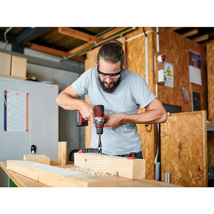Einhell Power X-Change 18V Akku-Bohrschrauber TE-CD 18 Li Brushless-Solo - 18 V, Ohne Akku - Mann bohrt mit einem Einhell Akku-Bohrschrauber ein Loch in ein Stück Holz, das mit einer Klemme befestigt ist.