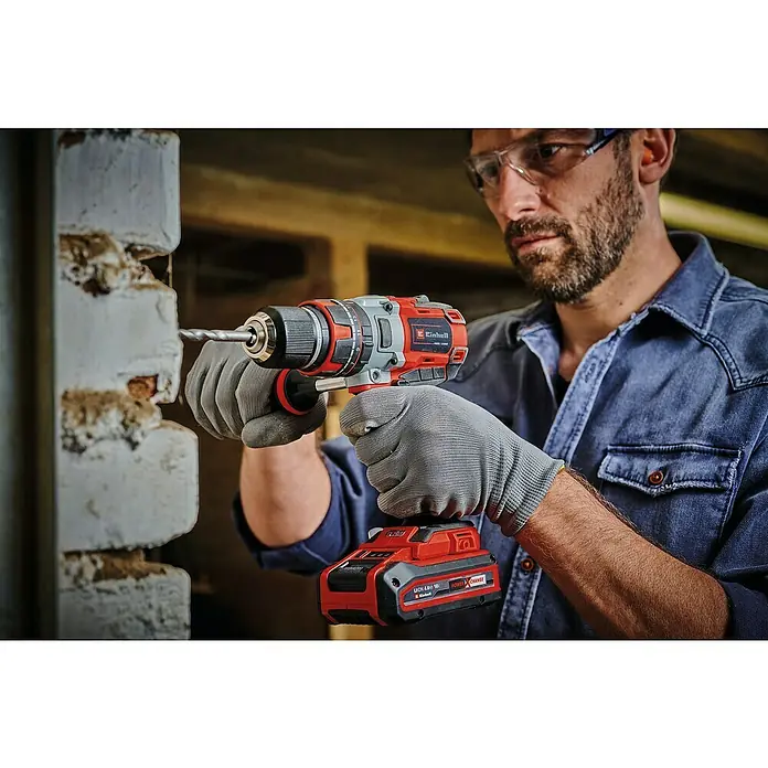 Einhell Professional Power X-Change 18V Akku-Schlagbohrschrauber TE-CD 18 Li-i Brushless-Solo - 18 V, Ohne Akku, 60 Nm - Ein Handwerker bohrt mit einem Einhell Akku-Bohrschrauber eine Ziegelwand, geschützt durch Brille und Handschuhe.