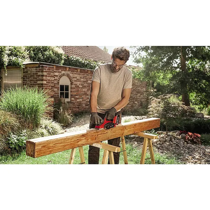 Einhell Power X-Change 18V Akku-Hobel TE-PL 18/82 Li-Solo - 18 V, Ohne Akku, Max. Leerlaufdrehzahl: 15.000 U/min - Mann hobelt Holzbalken im Freien mit Einhell Elektrohobel. Staub wirbelt in der Luft, während er mit der Maschine arbeitet.
