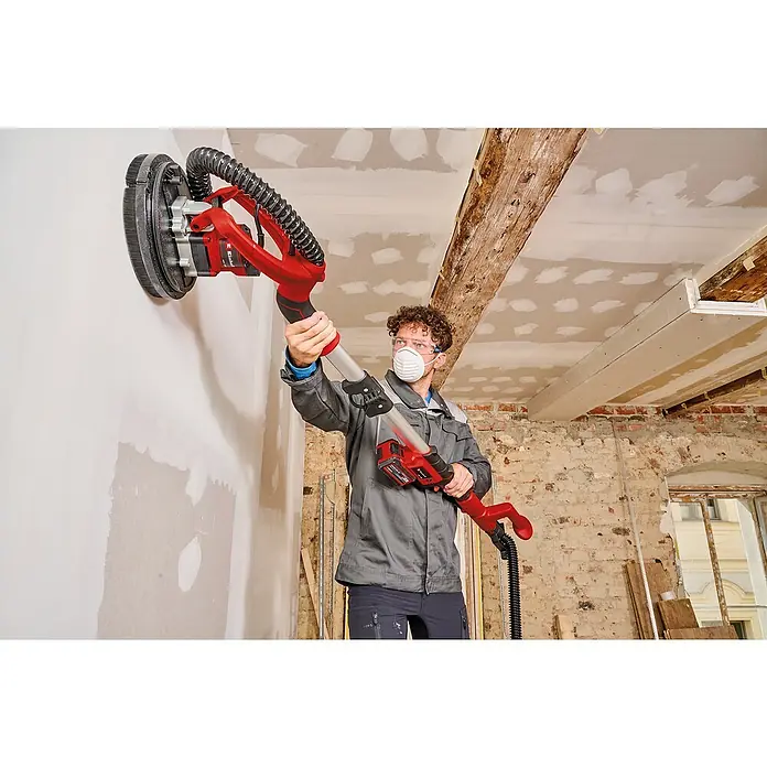 Einhell Professional PXC 18V Lijadora de pared y techo de batería TP-DW 18/225 Li - 18 V, Sin batería, Diámetro muela abrasiva: 225 mm - Un hombre usa una lijadora de paneles de yeso Einhell para lijar una pared. El dispositivo es rojo y tiene un mango largo.