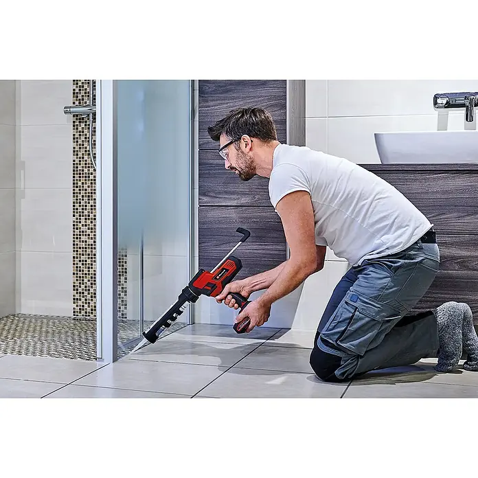 Einhell Power X-Change 18V Akku-Kartuschenpresse TE-SG 18/10 Li-Solo - 18 V, Ohne Akku - Mann dichtet mit einer Einhell Akku-Kartuschenpistole eine Duschkabine ab. Das Gerät ermöglicht präzises und müheloses Arbeiten im Bad.