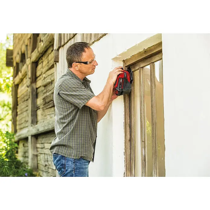 Einhell Power X-Change 18V Akku-Deltaschleifer TE-OS 18/150 Li Solo - 18 V, Ohne Akku, 24.000 U/min - Ein Mann mit Schutzbrille benutzt ein Einhell Multifunktionswerkzeug zum Schleifen eines Fensterrahmens im Freien.