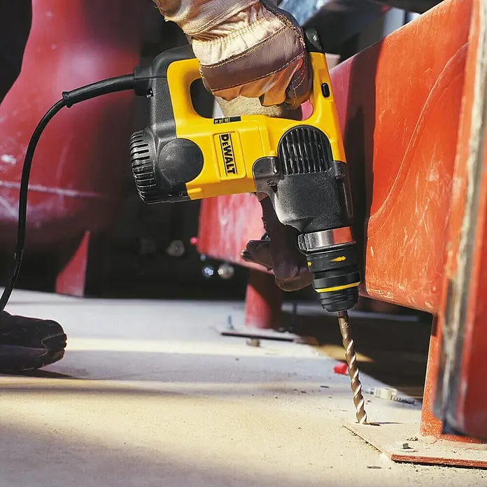 DeWalt Broca para hormigón y mampostería DT9566-QZ - 1 ud., Diámetro de la broca: 14 mm - Un martillo perforador DeWalt amarillo está siendo utilizado por una persona con guantes para perforar un agujero en una superficie de hormigón.