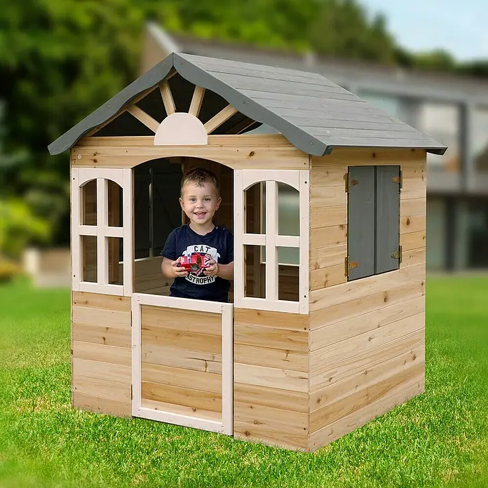 Dobar Spielhaus - L x B x H: 115 x 102 x 129 cm, Holz, Naturbelassen/Anthrazit - Ein Junge steht in einem Holzspielhaus mit grauem Dach und weißen Fenstern. Das Spielhaus steht auf einer grünen Wiese.